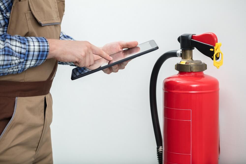 Close-up Of Technician Using Digital Tablet Checking Fire Extinguisher